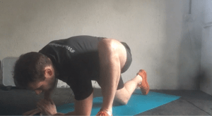 Fitness instructor demonstrates the second stage of the hip opener stretch by taking a lunge position and reaching towards the floor with the same elbow as the front leg